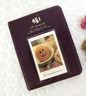 A dark purple compact photo album with a gold embossed design featuring a smiling face illustration.
