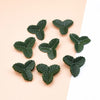 A collection of small, dark green silk artificial leaves scattered on a light pink background.