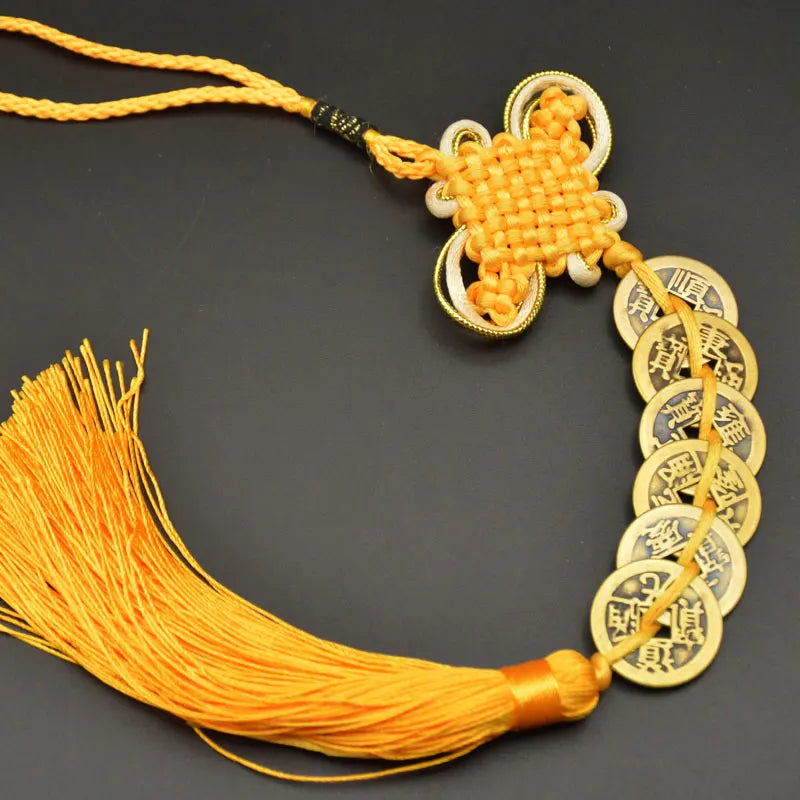 A golden I Ching copper coin feng shui charm with a handwoven knot and orange silk tassel.