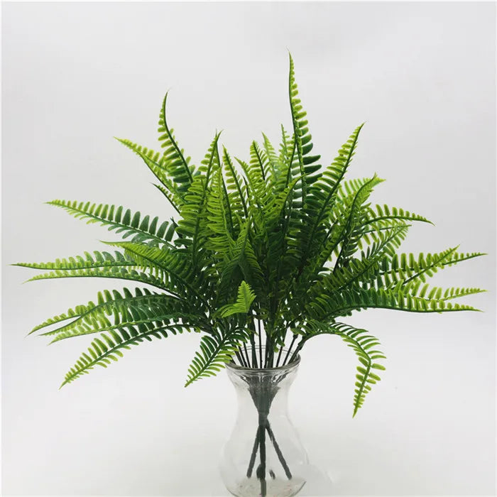 A vibrant green artificial fern with delicate fronds displayed in a clear glass vase.
