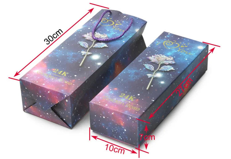 A rectangular box containing a 24k gold foil artificial rose bouquet with a purple ribbon, shown at an angle.
