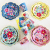 A collection of colorful floral disposable tableware including plates, cups, and napkins in shades of blue, pink, yellow, and