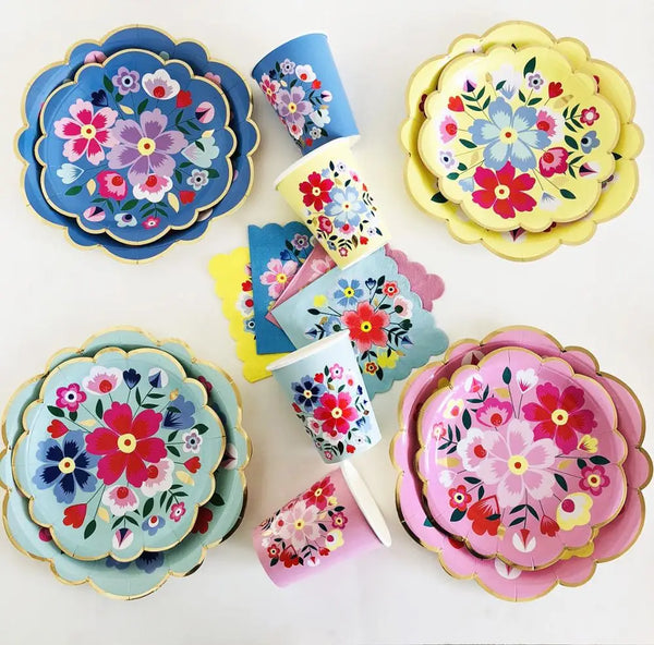 A collection of colorful floral disposable tableware including plates, cups, and napkins in shades of blue, pink, yellow, and