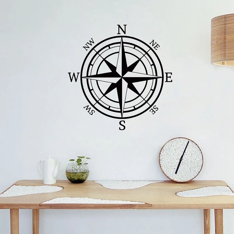 A black nautical compass rose decal is mounted on a white wall above a wooden table.