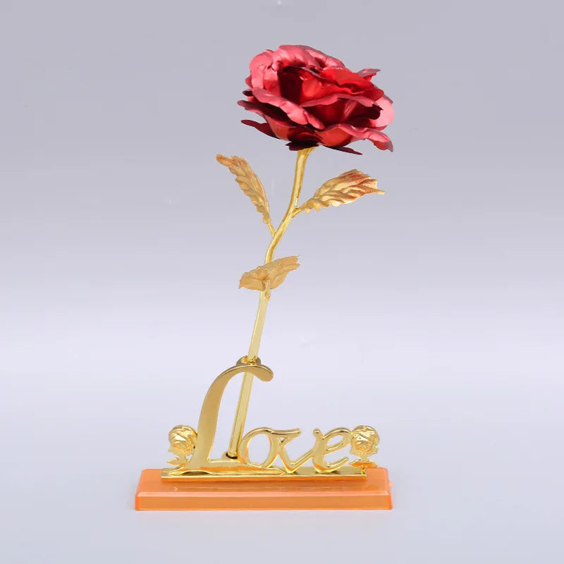 A gold foil artificial rose with a stem and leaves stands on a base engraved with the word love.