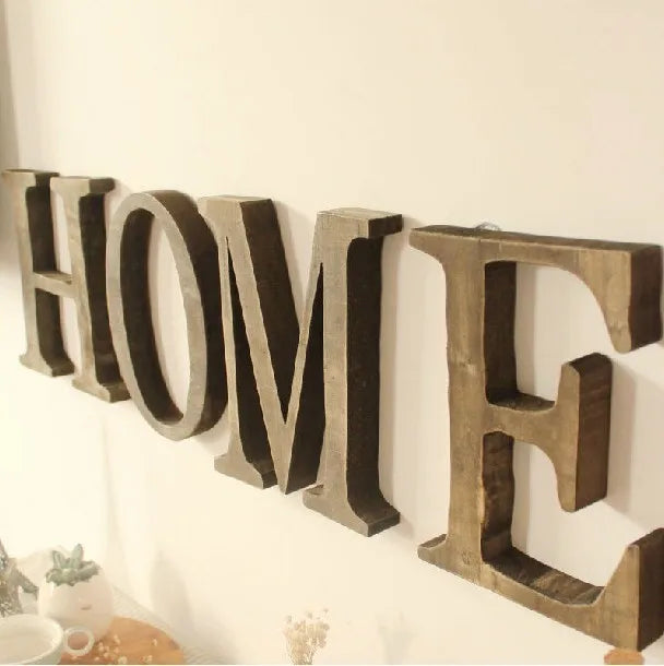 A row of vintage wooden alphabet letters spelling HOME mounted on a white wall.