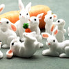 A collection of white miniature rabbit figurines, some with orange carrots, arranged on a green surface.