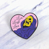 A heart-shaped enamel pin featuring a yellow skull wearing a purple hood with the text Live Laugh Love.