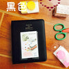 A black compact photo album for instant film is displayed on a wooden surface next to yellow and red heart decorations.