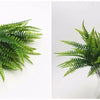 A sprig of vibrant green artificial fern leaves displayed in a clear glass vase.