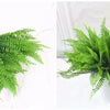 A sprig of bright green artificial fern leaves and fronds displayed on a white marble surface.