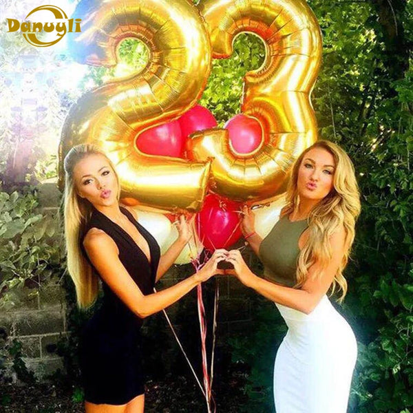 Two women posing with large rose gold foil number balloons spelling out 23 in a green outdoor setting