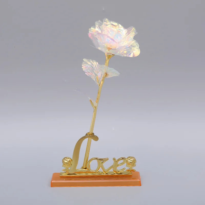 A delicate gold foil artificial rose bouquet with a pink and white flower on a slender stem, mounted on an orange base.