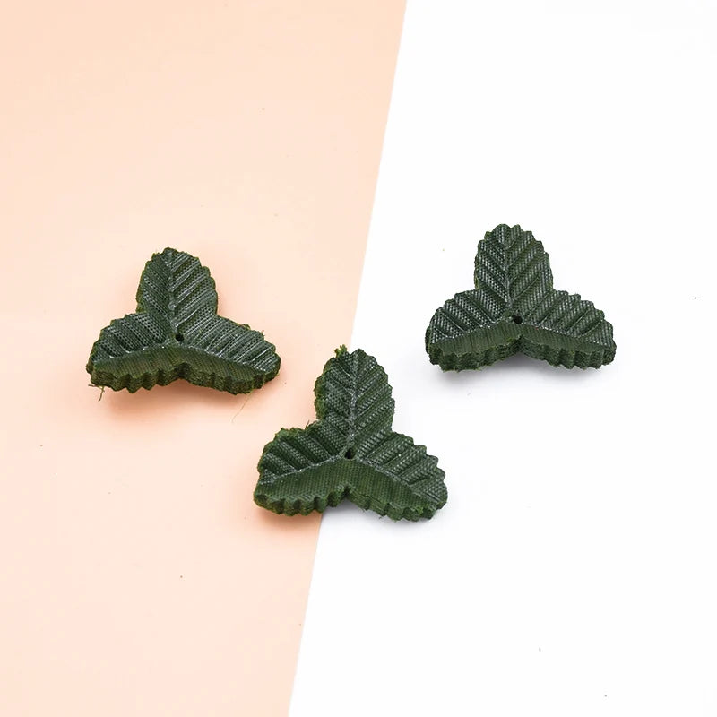 Three artificial green leaves for crafts and home decor displayed on a light pink background.