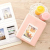 A pink compact photo album with a lid displaying instant film photos and a yellow candle.