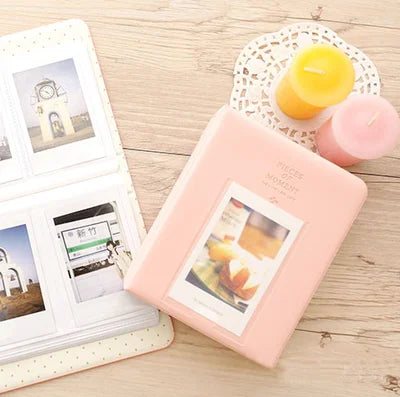 A pink compact photo album with a lid displaying instant film photos and a yellow candle.