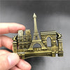 Une main tient une réplique décorative en métal de la Tour Eiffel et les mots PARTS comme aimants de réfrigérateur.