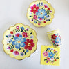 A set of yellow floral disposable tableware including a plate, a cup, and a napkin.