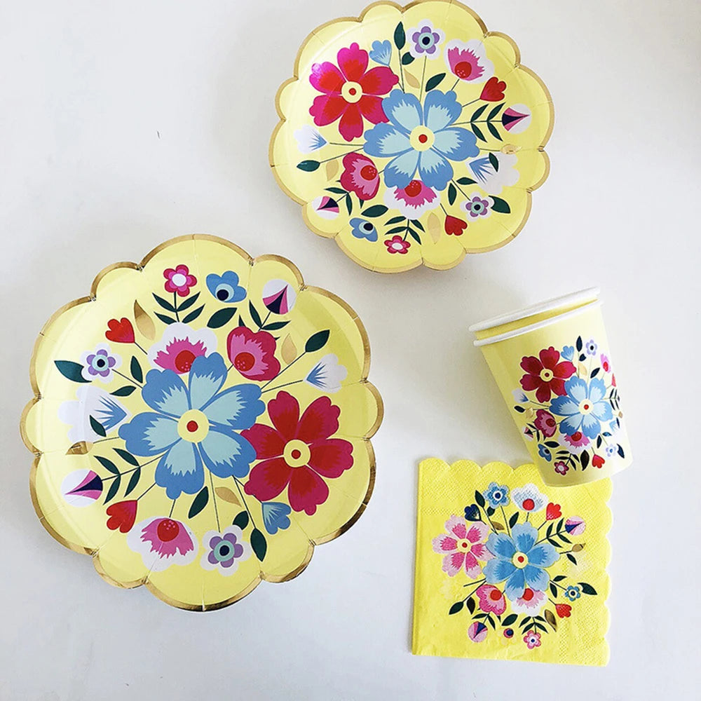 A set of yellow floral disposable tableware including a plate, a cup, and a napkin.