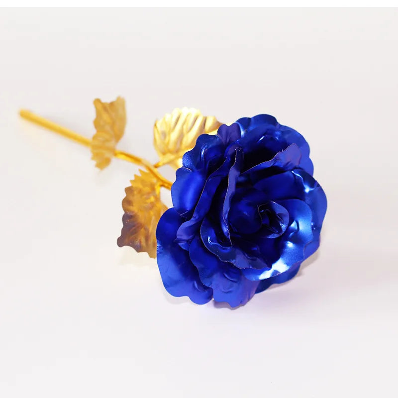 A deep blue artificial rose with gold foil leaves on a white background.