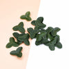 A scattered pile of artificial green leaves used for crafts and home decor on a light background.