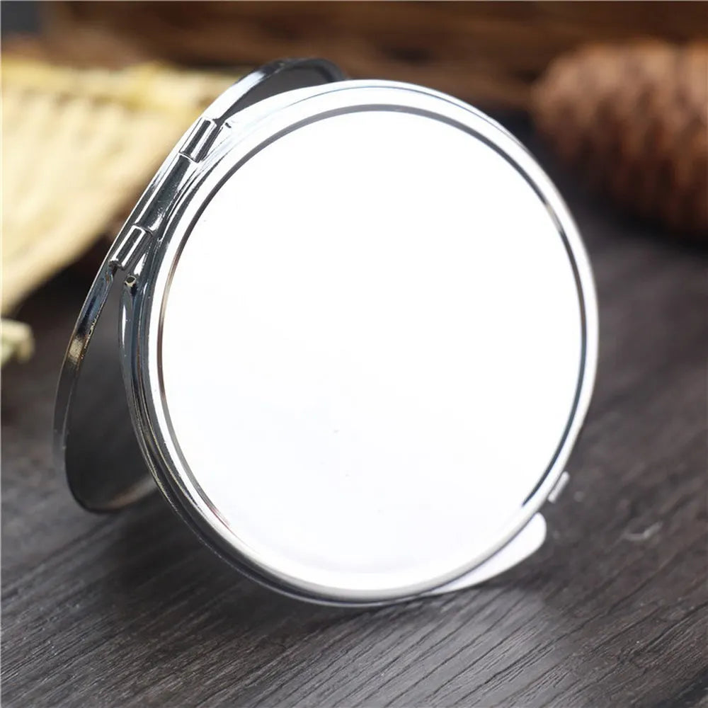 A silver mini double-sided folding makeup mirror is shown resting on a dark wooden surface.