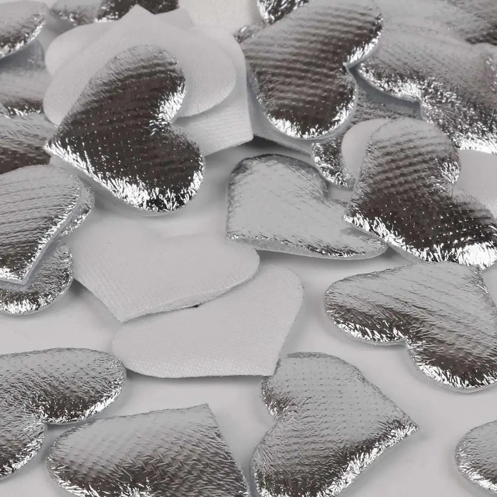 Silver heart-shaped sponge confetti pieces scattered on a white surface