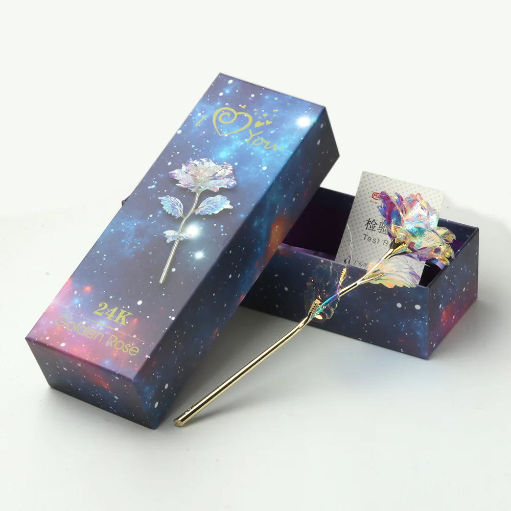 A rectangular box with a dark blue background and gold foil detailing holds a delicate artificial rose flower.