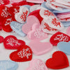 A variety of heart-shaped sponge confetti in red, pink, and blue colors scattered on a white surface.
