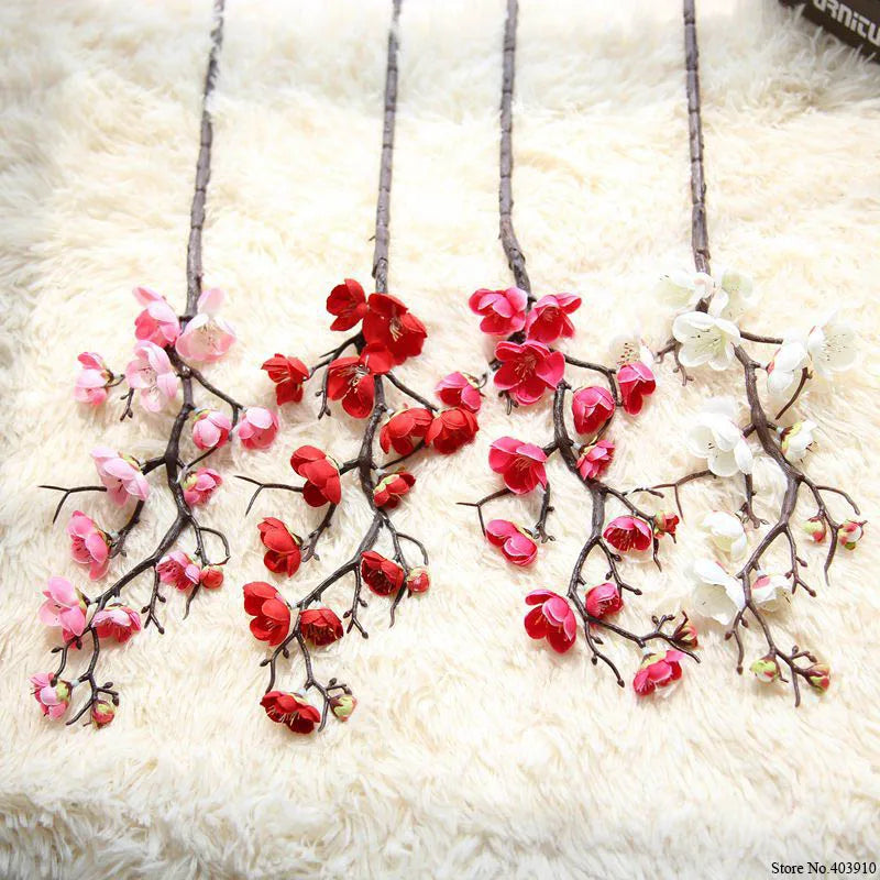 Artificial silk cherry blossom branches with pink and red flowers displayed on a white fluffy surface.