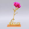 A gold foil artificial rose with a pink bloom and the word Love on a stand.