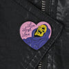 A heart-shaped enamel pin featuring a yellow skull design with the text Live Laugh Love on a purple background.