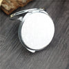 A small, round, silver-framed folding makeup mirror with an intricate design resting on a dark wooden surface.