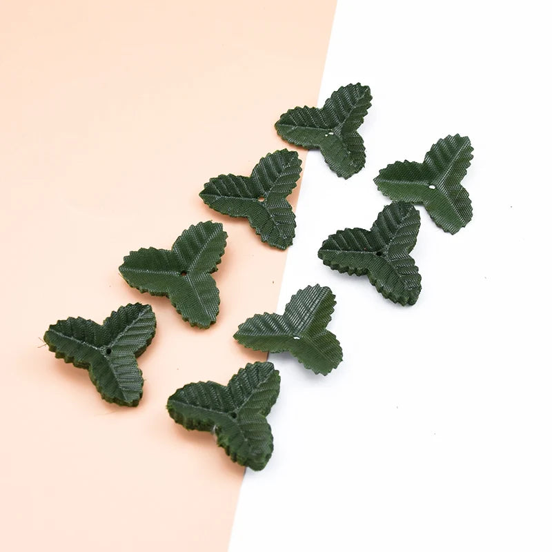 A collection of small, dark green silk artificial leaves scattered on a light pink and white background.