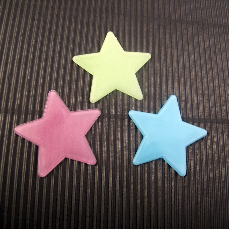 Three glow-in-the-dark star wall stickers in yellow, pink, and blue against a dark background.