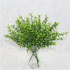 A glass vase filled with artificial green fern and leaf sprigs for home decor
