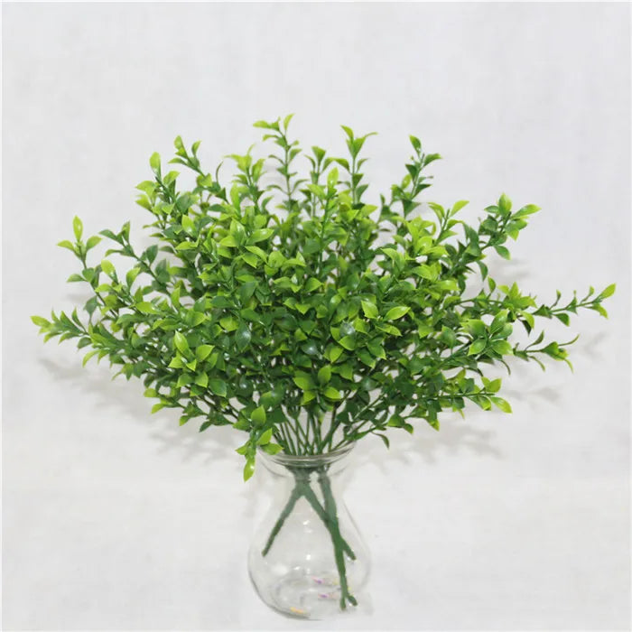 A glass vase filled with artificial green fern and leaf sprigs for home decor