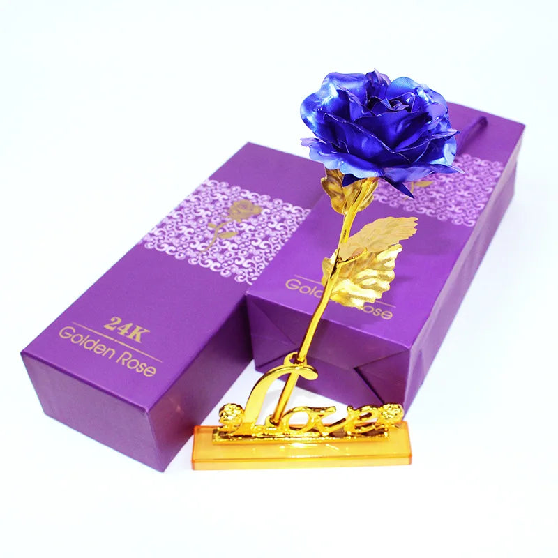 A purple box containing a blue artificial rose with a gold foil stem and leaf.