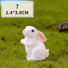 A white miniature rabbit figurine sitting on green grass. The product size is 7 by 2.4 x 3.0 cm.