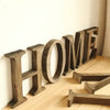 A row of rustic wooden alphabet letters spelling HOME displayed on a light wooden floor.