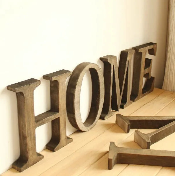A row of rustic wooden alphabet letters spelling HOME displayed on a light wooden floor.