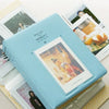 A light blue compact photo album with a textured cover lying next to several instant film photos.