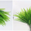 A close-up of bright green artificial fern and leaf sprigs arranged in a glass vase.