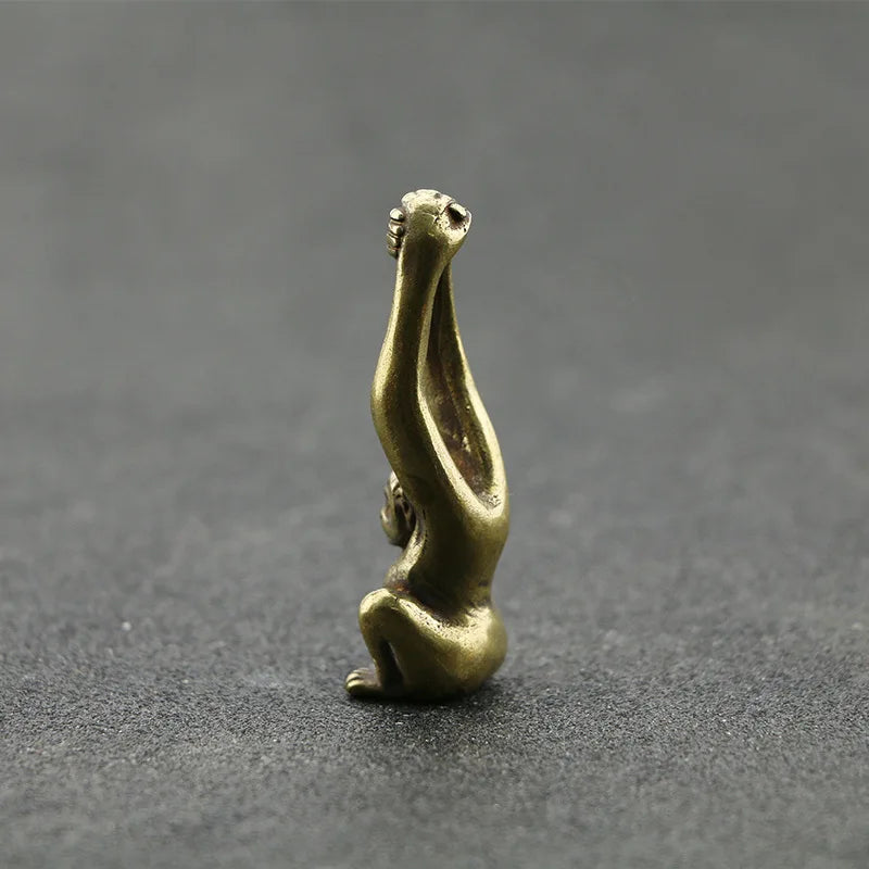 A vintage brass monkey key chain charm shaped like a monkey, resting on a dark gray surface.