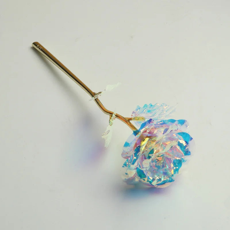 A delicate artificial rose bouquet with blue and pink petals attached to a thin gold foil stem.