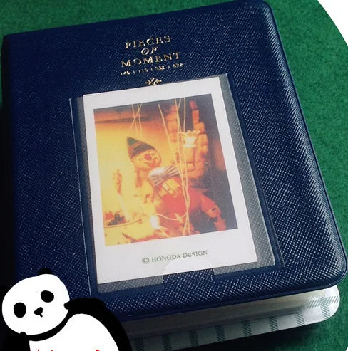A dark blue compact photo album with a gold embossed title and an open view of instant film photos inside.