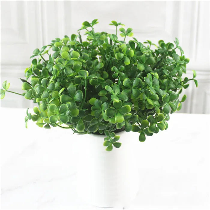 A vibrant green artificial fern and leaf sprig arrangement in a white pot for home decor.