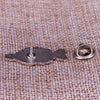 A silver enamel pin shaped like a fish resting on a textured fabric surface.