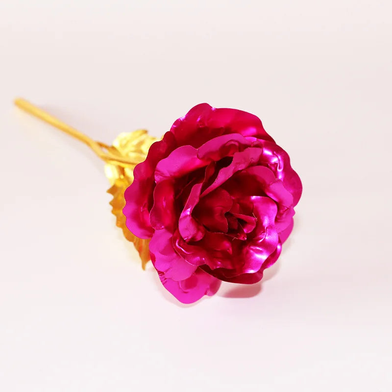 A deep magenta artificial rose with a gold foil stem against a white background.