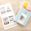 A light blue compact photo album with a lid open, displaying instant film photos and next to a yellow candle.